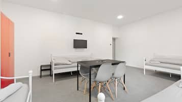 Une chambre moderne avec un lit, une table et des chaises, un téléviseur fixé au mur et une armoire rouge.