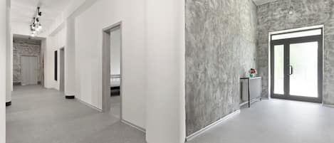 Un pasillo espacioso con diseño moderno, que presenta una pared de acento de concreto, un radiador y una puerta que conduce a otra habitación.