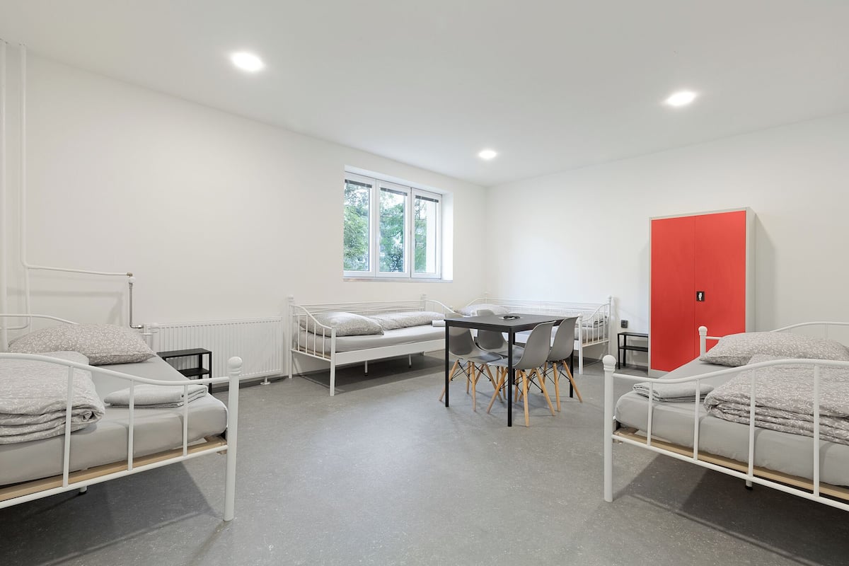 A room with two beds, a table, and a red wardrobe.