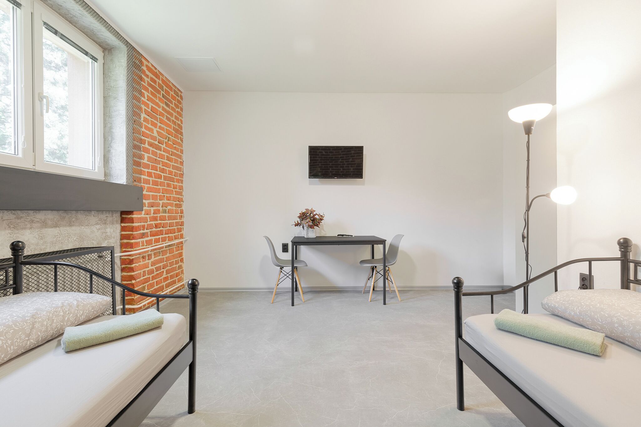 Ein modernes Zimmer mit einer Ziegelwand, einem Schreibtisch mit zwei Stühlen und einem Bett mit Kopfkissen und Decke.