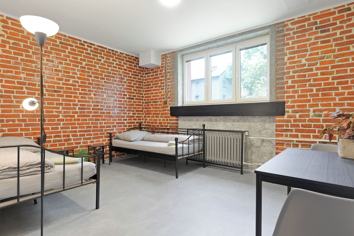 A room with a brick wall, a bed, a table, and a window.