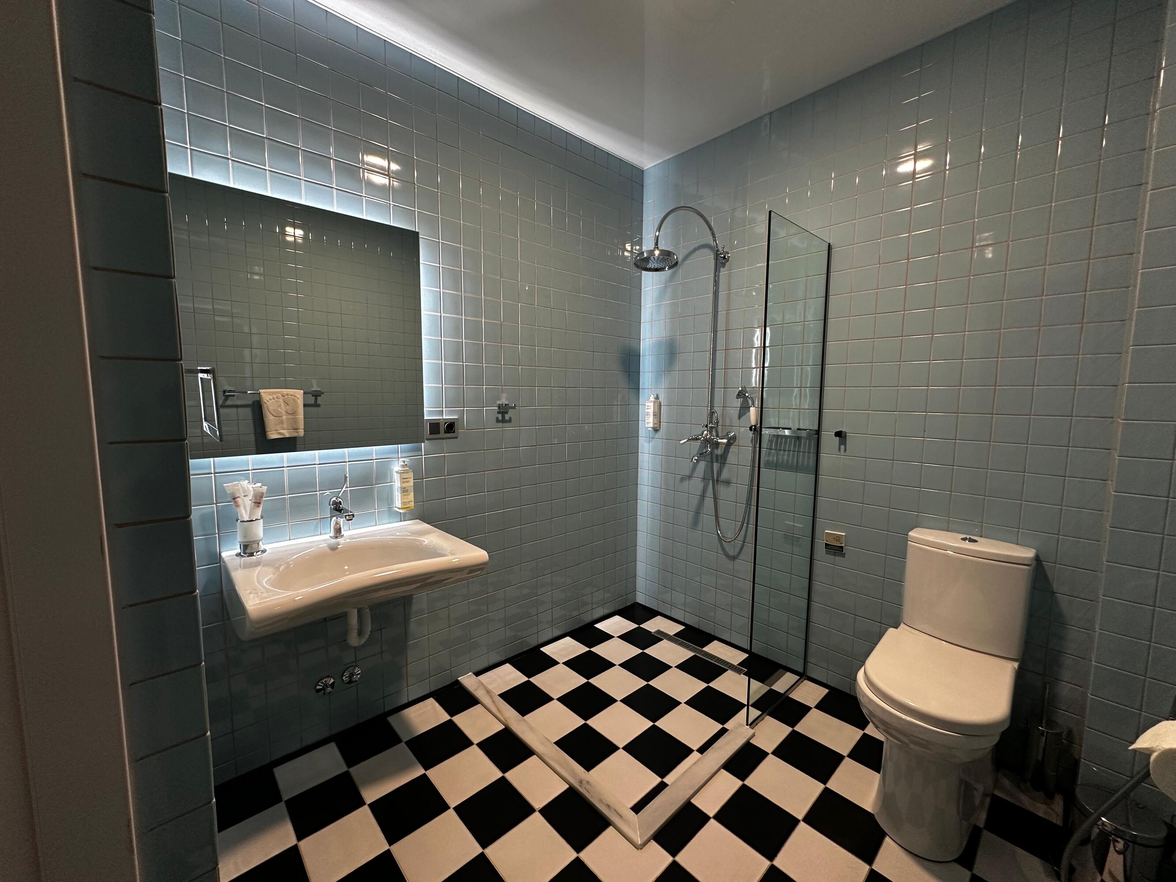 Une salle de bain avec un lavabo, des toilettes et une douche. Le sol est recouvert d’un motif à carreaux noirs et blancs.
