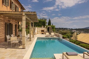 Una piscina con sillones de descanso, una pérgola y un muro de piedra.