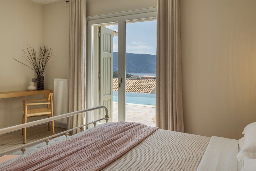 Une chambre d’hôtel avec un lit, une chaise, une table de chevet, une fenêtre avec des rideaux et une vue sur une piscine et des montagnes.