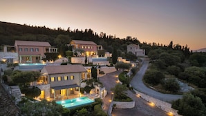 Une villa située sur une colline, comprenant plusieurs bâtiments, une piscine et un chemin sinueux.