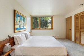 A bedroom with a bed, a window, a painting, a bedside lamp, a bedside table, and a closet.