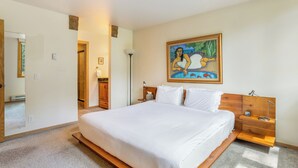 Hotellihuone, jossa on suuri sänky, puinen pääty, yöpöydät, pieni sivupöytä, seinällä oleva taulu ja ovi, joka johtaa toiseen huoneeseen.