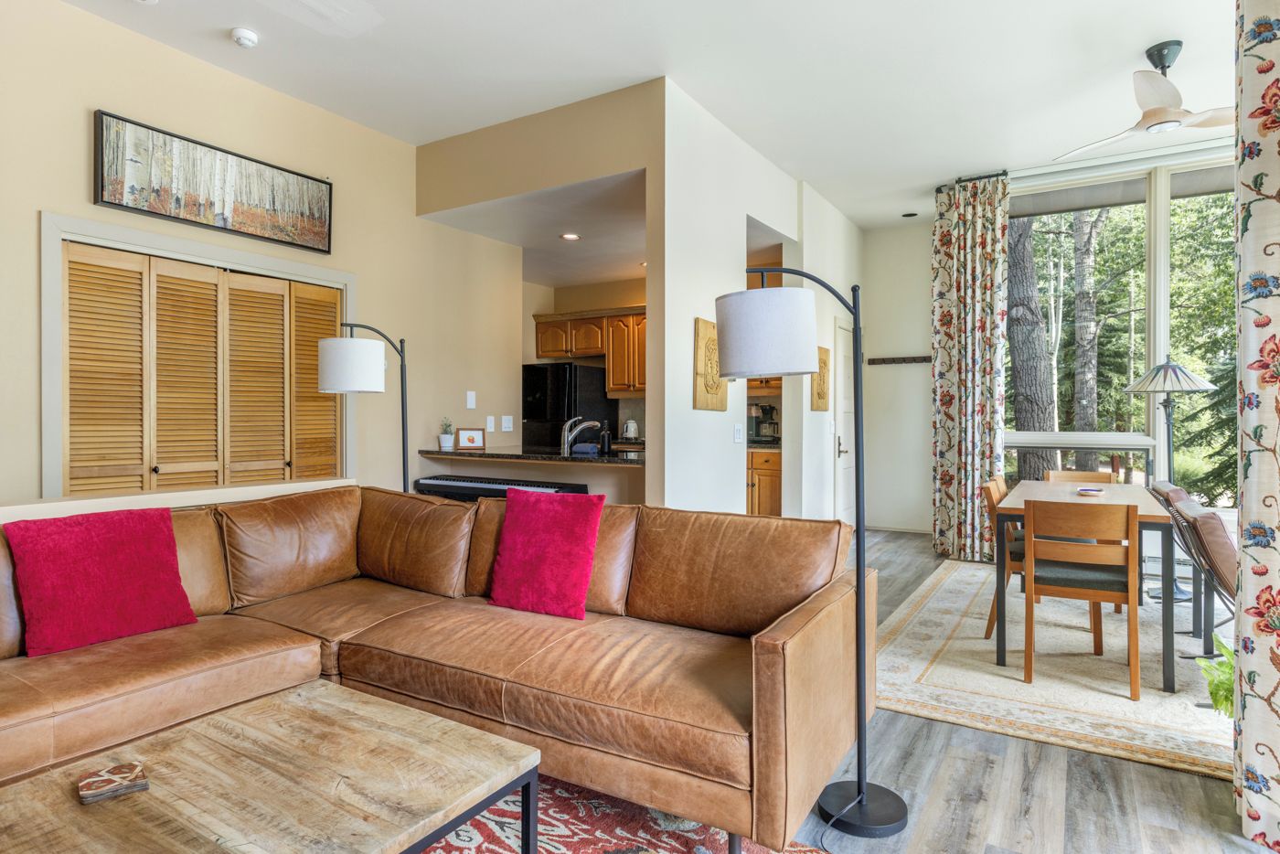 A living room with a brown leather sofa, a coffee table, and a dining area with a table and chairs.