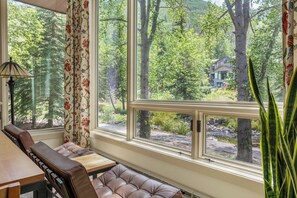 A room with a large window, a cushioned bench, and a table.