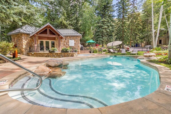 A pool area with a stone building, lounge chairs, and a clear blue pool.