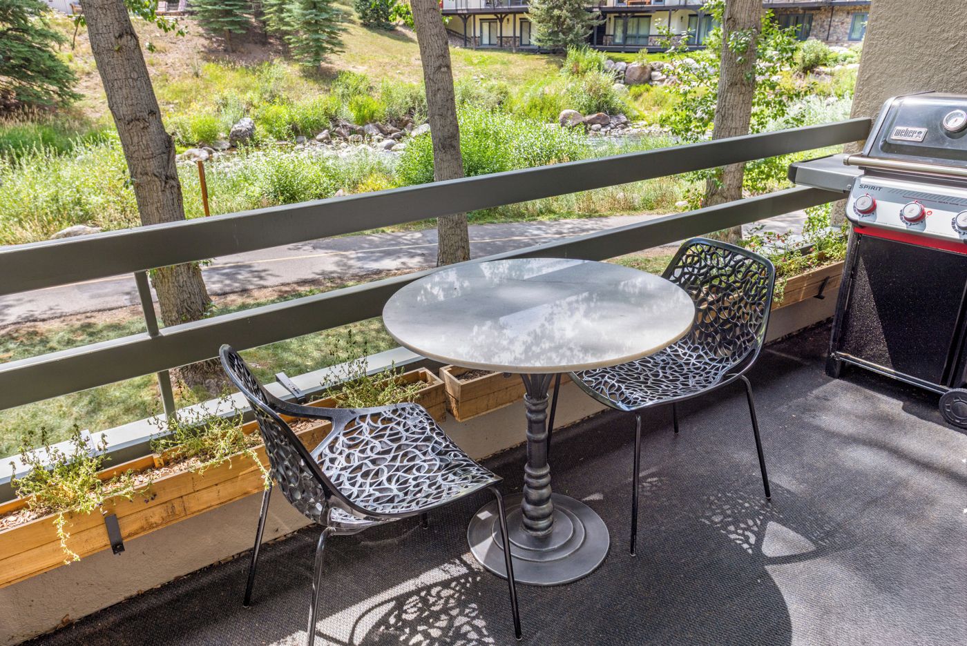En uteplats med ett runt bord och två stolar, en grill och utsikt över ett bostadsområde.