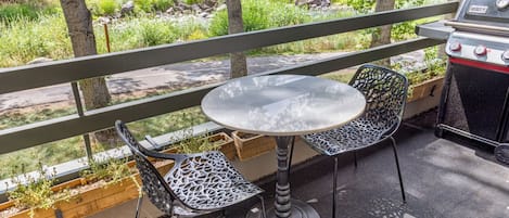 En uteplats med ett runt bord och två stolar, en grill och utsikt över ett bostadsområde.