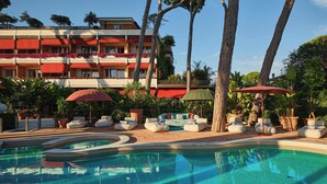 Un hotel con piscina, mobiliario exterior y jardines tropicales.
