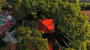 Vista aérea de una propiedad con piscina, zona de estar y una estructura de techo rojo rodeada de abundante vegetación.