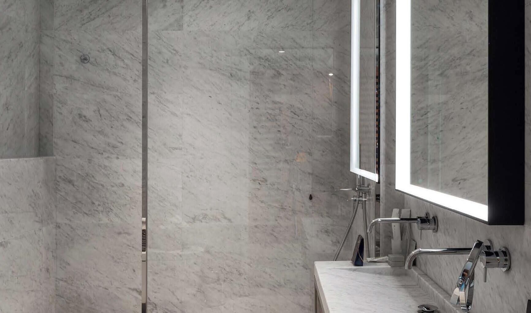A modern bathroom with a marble floor, a glass shower enclosure, a large mirror, and a sink with a chrome faucet.
