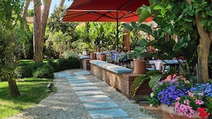 Un patio jardín con mesas, un paraguas rojo y un sendero de grava.