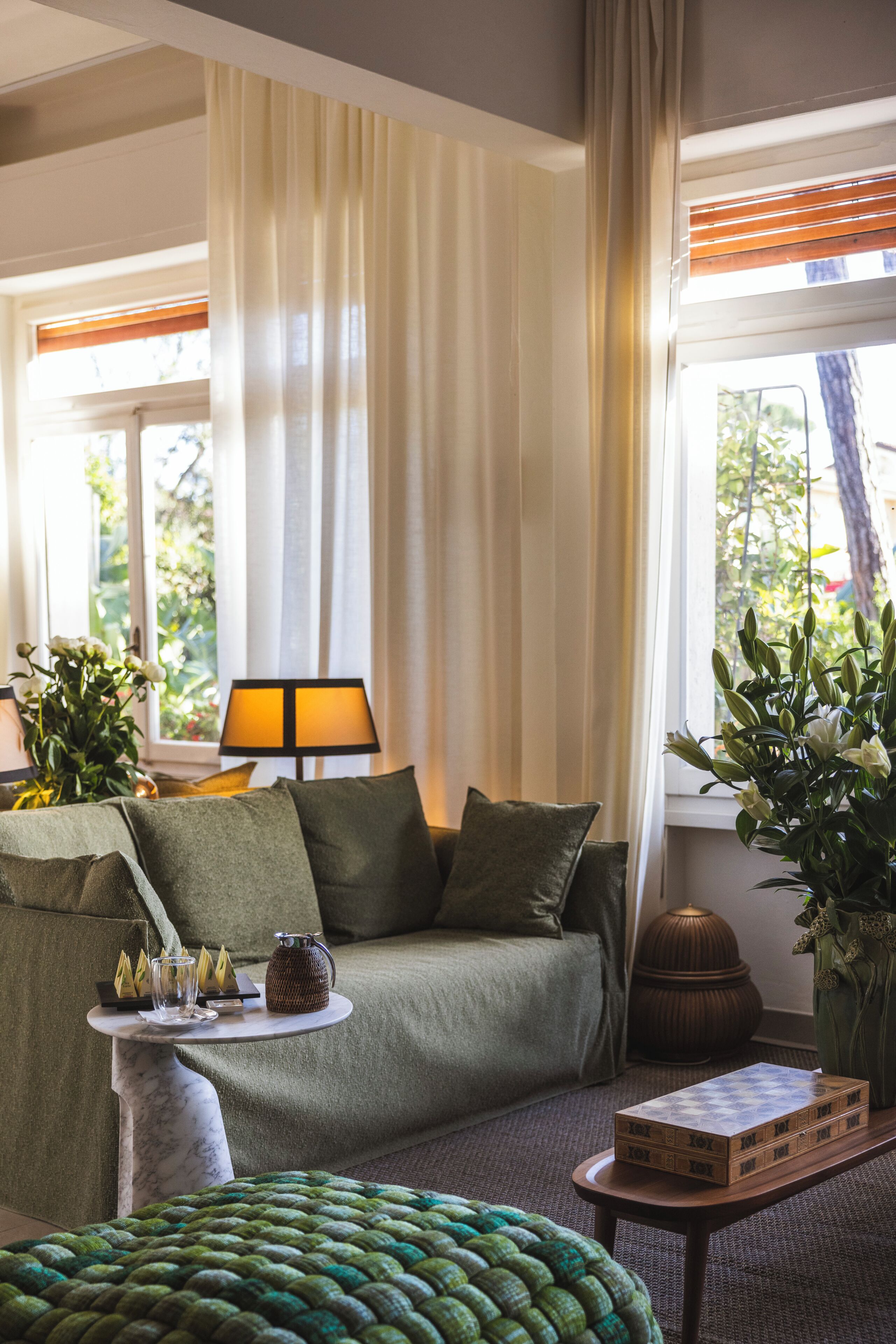 Ein gemütliches Zimmer mit einer Couch, einem kleinen Tisch, einer Lampe und einem Fenster mit Vorhängen.