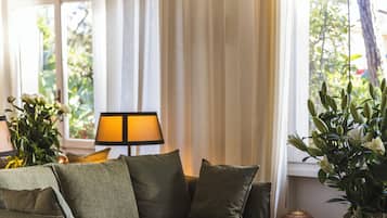 Ein gemütliches Zimmer mit einer Couch, einem kleinen Tisch, einer Lampe und einem Fenster mit Vorhängen.