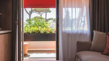 A room with a bed, a window with curtains, a view of greenery outside, and a red awning.