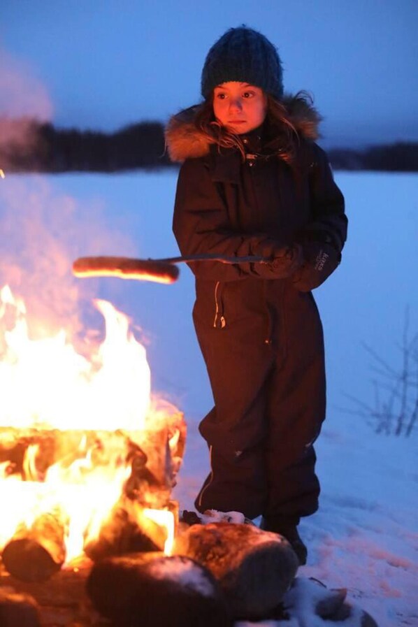 A person standing by a campfire in a snowy outdoor setting. - Cozy Stuga With Mountain & Northern Lights View (Ramsele)