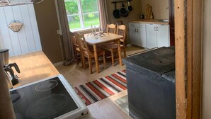 Une cuisine de taille réduite, équipée d’une cuisinière, d’une table à manger avec des chaises et d’une fenêtre avec des rideaux.