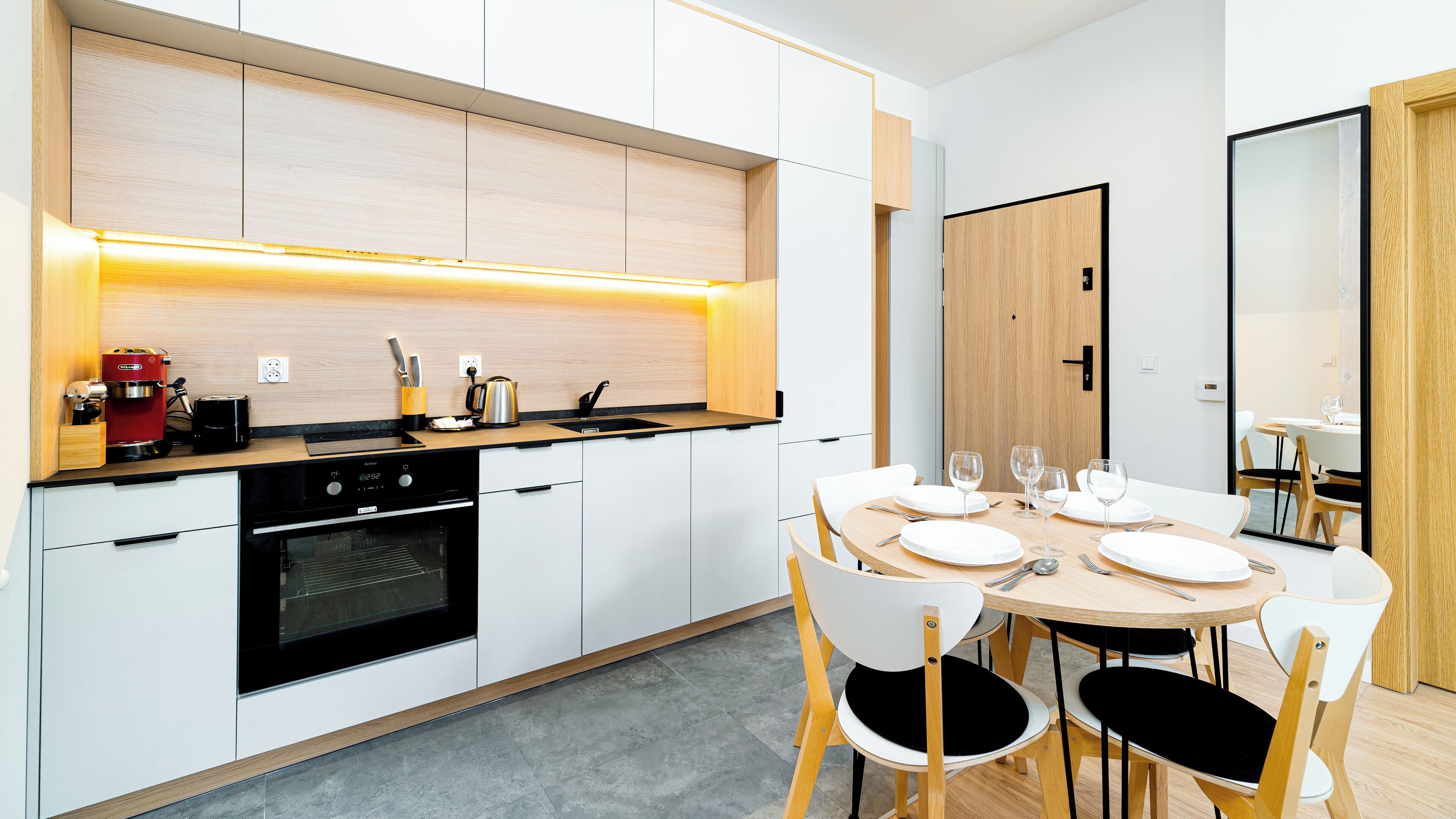 A modern kitchen with a built-in oven, a coffee machine, and a dining area with a round table and chairs.