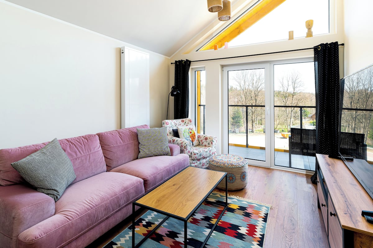 Een moderne woonkamer met een roze bank, een houten bijzettafeltje en een kleurrijk vloerkleed.