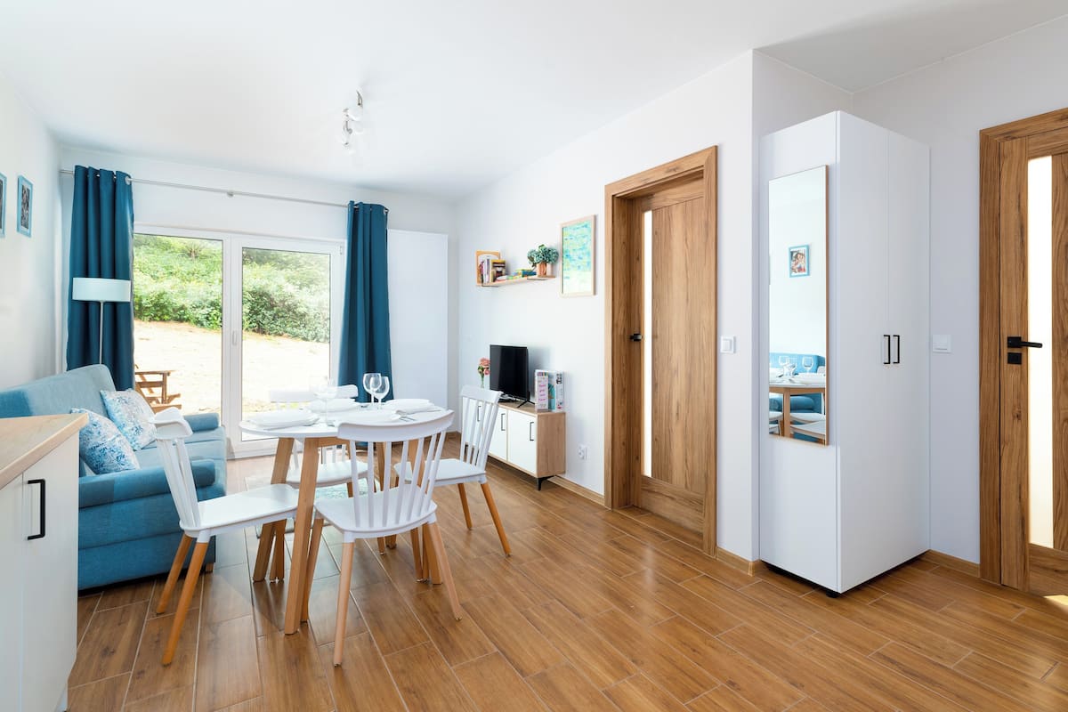 Een moderne woonkamer met een eethoek, houten vloeren en uitzicht op het groen.