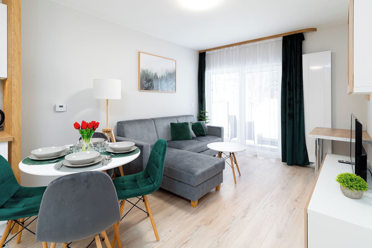 Een moderne woonkamer met een grijze bank, groene stoelen, een eettafel voor vier personen en een klein bijzettafeltje.