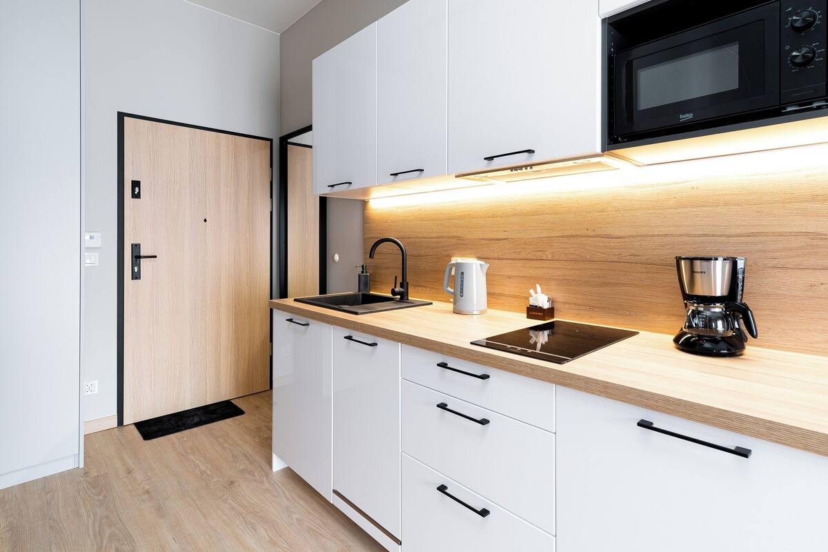 Een moderne keuken met witte kasten, een houten aanrecht, een zwarte spoelbak, een waterkoker, een koffiezetapparaat en een magnetron.