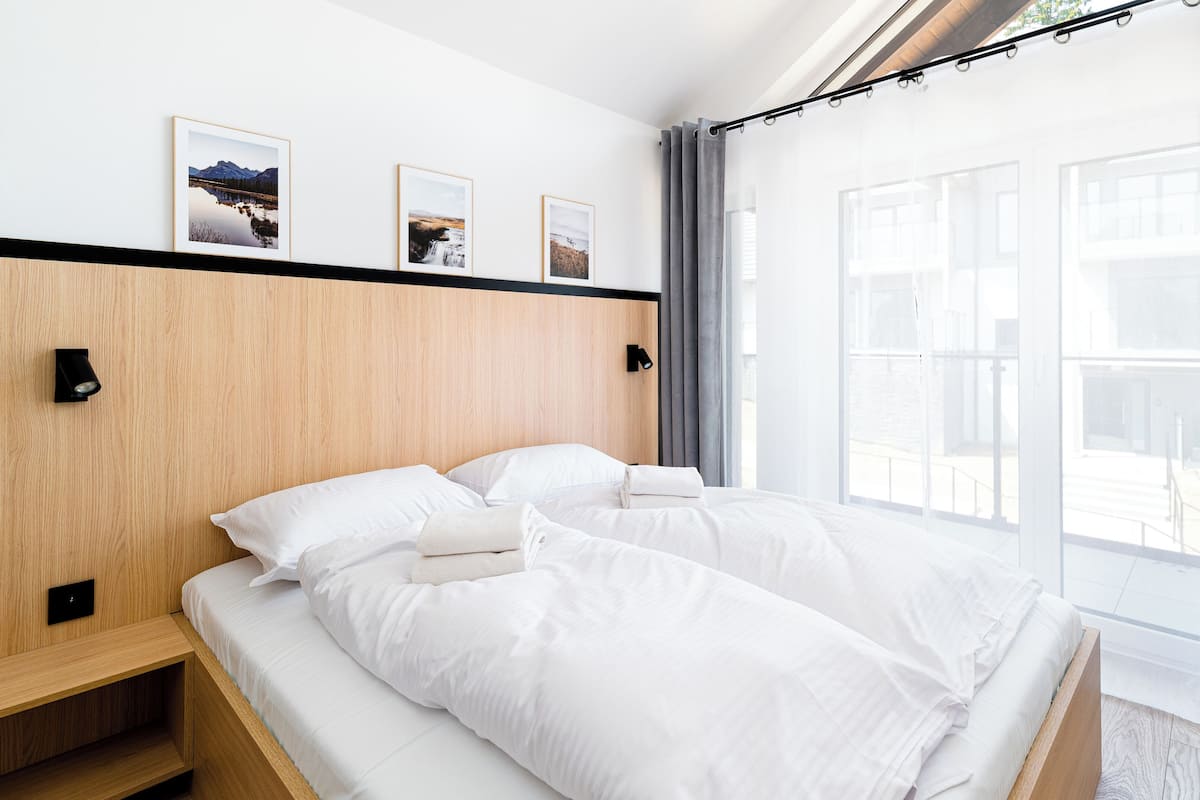 Een moderne hotelkamer met een houten hoofdbord, twee bedden, een klein nachtkastje van hout en een groot raam met gordijnen.