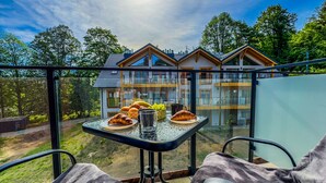 Parvekkeella on aamiainen katettuna, ja sieltä avautuu näkymä moderniin rakennukseen, jossa on useita ikkunoita, sekä kirkkaalle taivaalle.