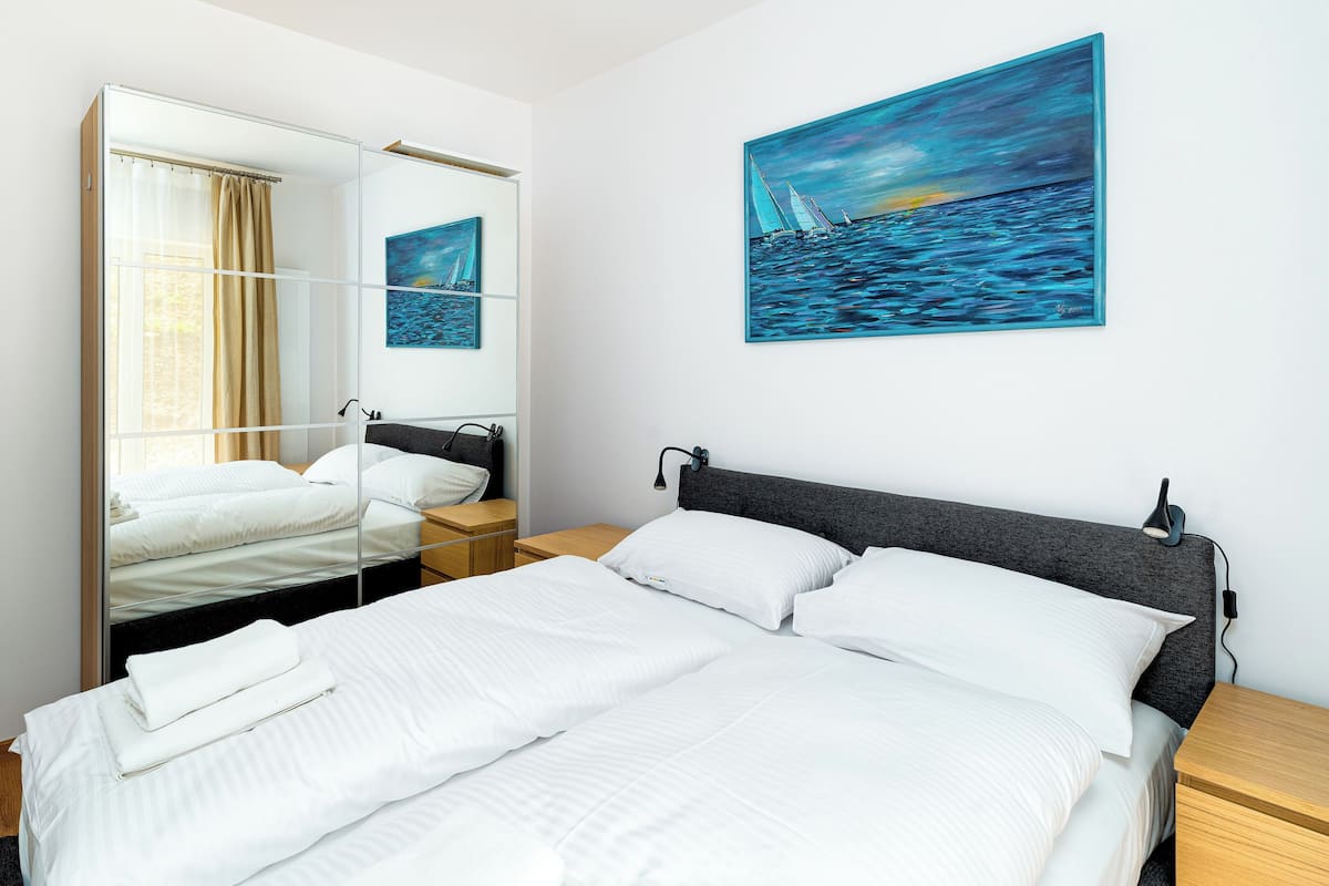 Een hotelkamer met een groot bed, een nachtkastje, een spiegel en een schilderij van een zeilboot aan de muur.