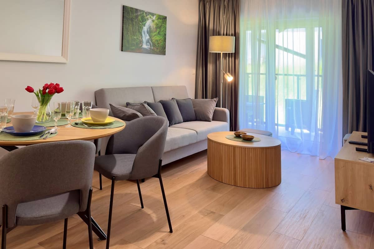 Een moderne woonkamer met een ronde houten eettafel, grijze banken en een houten salontafel.