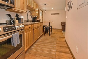 Una cocina con armarios de madera, un horno de acero inoxidable, un lavamanos y una zona de comedor con taburetes.