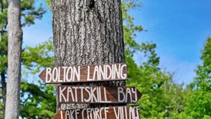 En träskylt med flera pilar som visar olika riktningar och pekar ut platser som Bolton Landing, Kattskill Bay och Harris Bay.