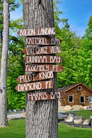 Un cartel de madera con varias flechas direccionales que indican diferentes lugares como Bolton Landing, Kattskill Bay y Harris Bay.