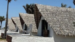 Thatched-roof huts with lounge chairs and a small table, surrounded by palm trees. - zaya lençois hotel (Santo Amaro do Maranhão)