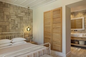 Slaapkamer met een stenen muur, een bed met wit beddengoed, een houten garderobe en een badkamer met een stenen muur en een houten vloer.