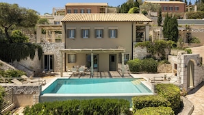 Una casa de dues plantes amb piscina, parets de pedra i un patí amb moble d'exterior.