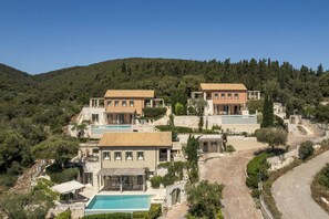 Ein Anwesen an einem Hang mit mehreren Gebäuden, einem Pool und einer kurvenreichen Auffahrt.