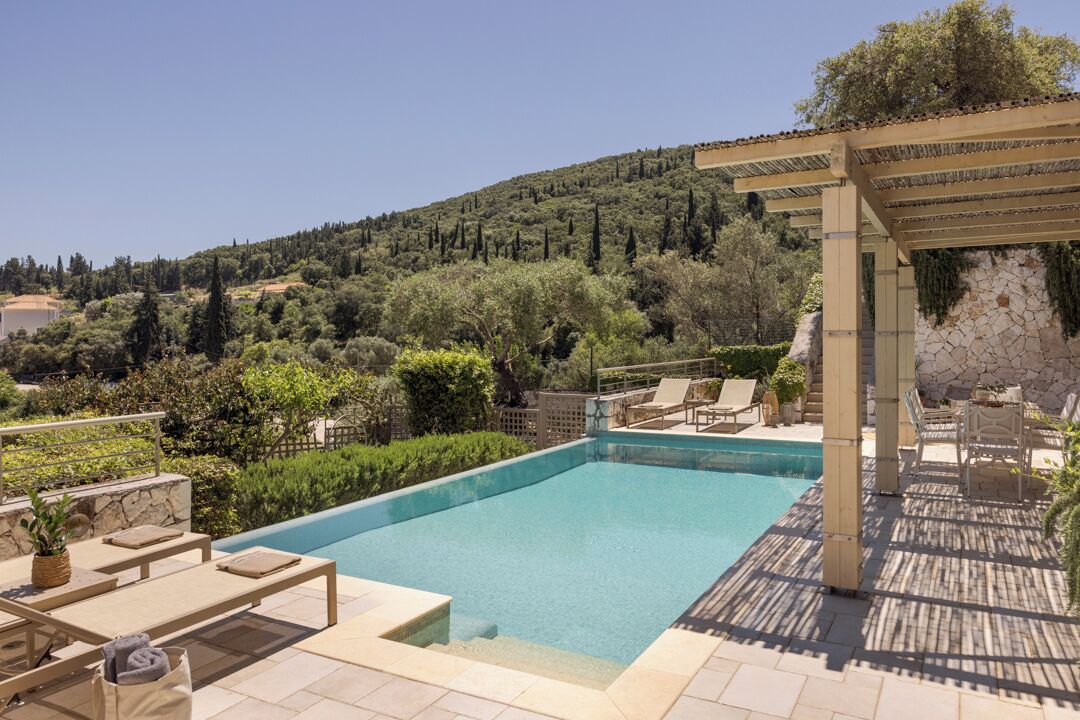 A swimming pool with lounge chairs, a pergola, and a view of a hilly landscape.