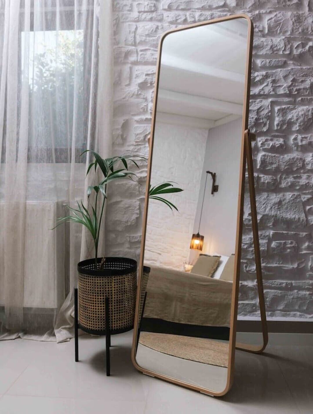 Une pièce avec un grand miroir, une plante en pot et un lit placé contre un mur à la texture particulière.