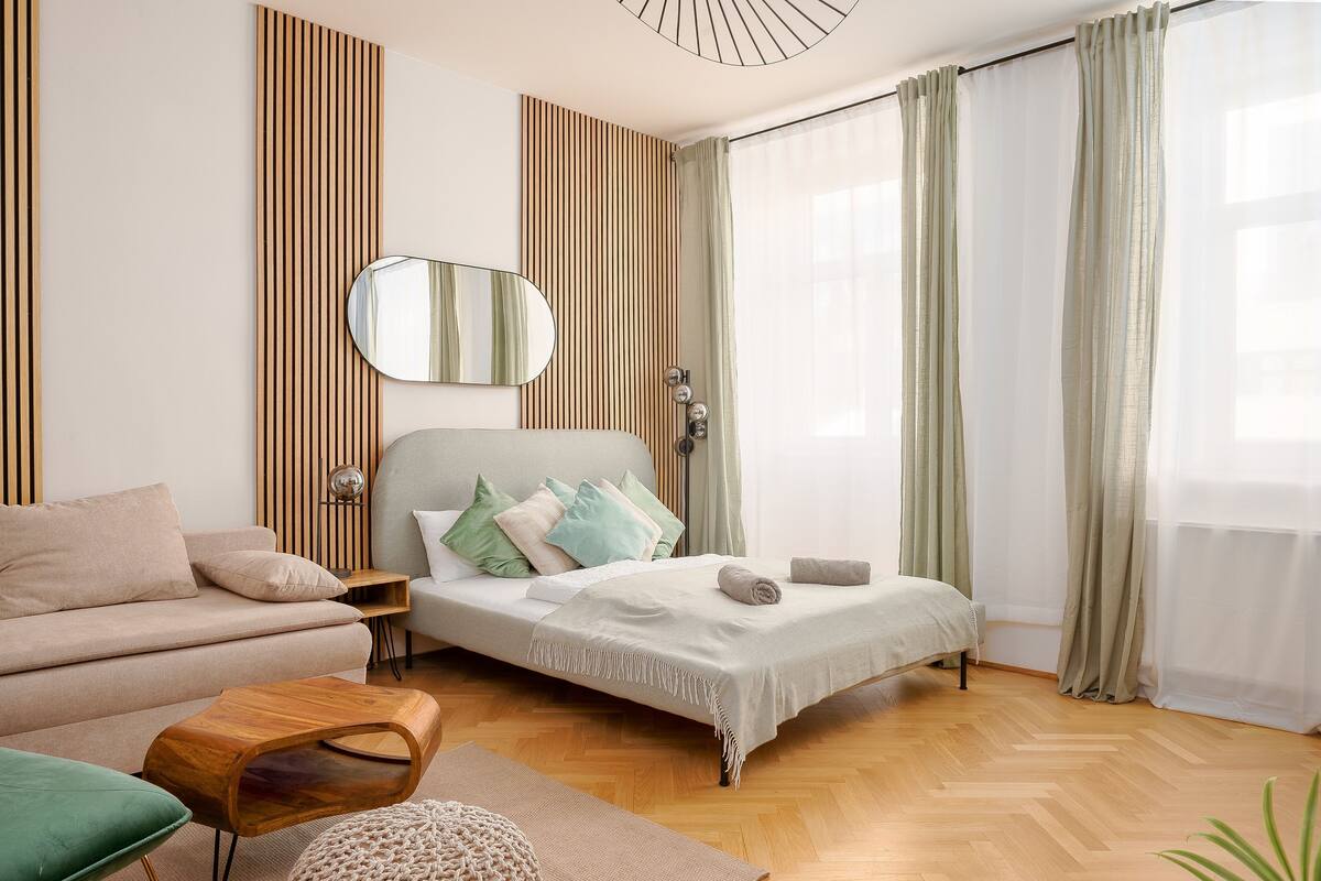 A modern bedroom with a bed, a sofa, a small table, and a mirror.