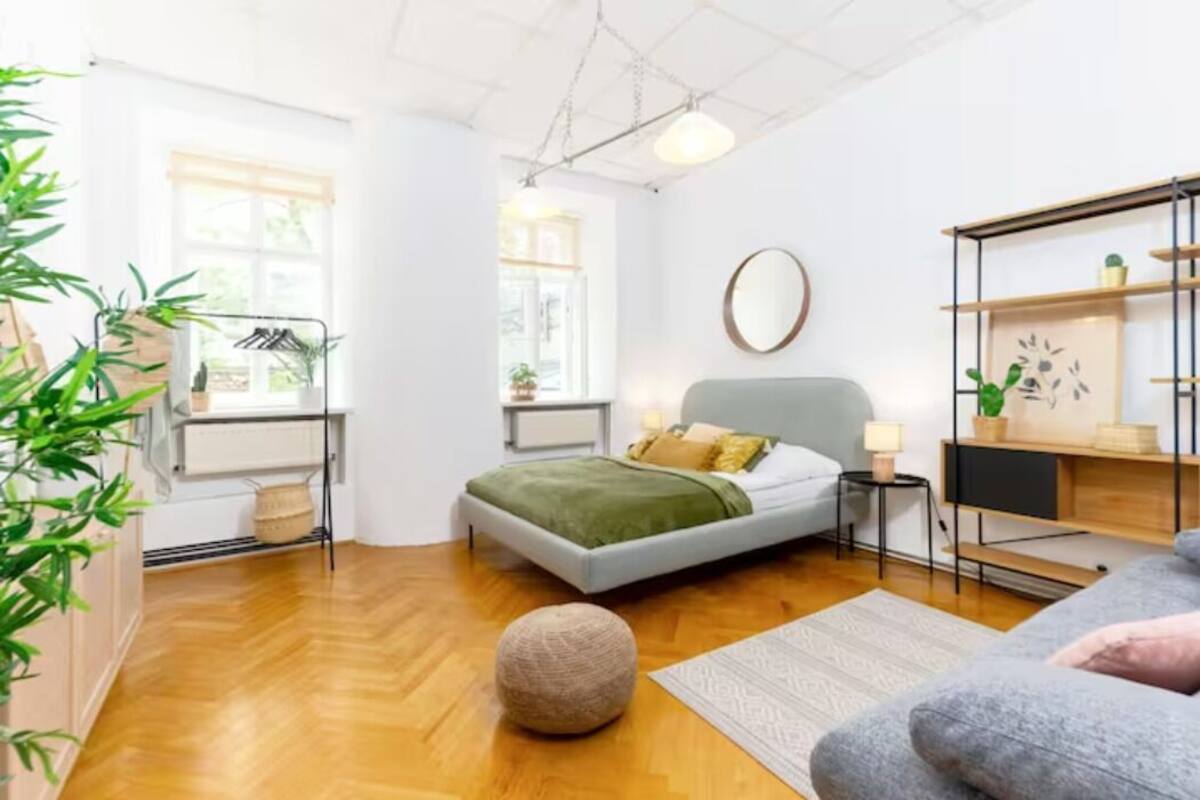 A modern bedroom with a bed, bedside tables, a lamp, a round mirror, and a shelving unit with plants.