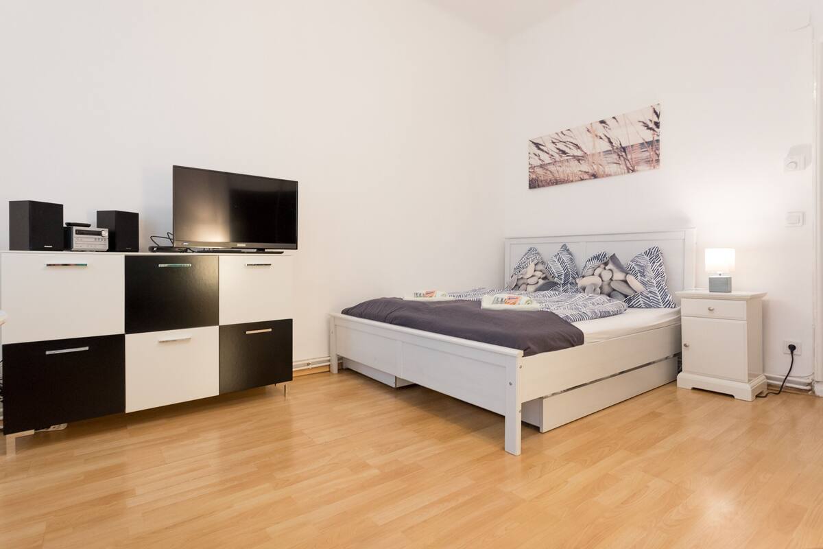 A modern bedroom with a bed, bedside table, TV, and storage unit.