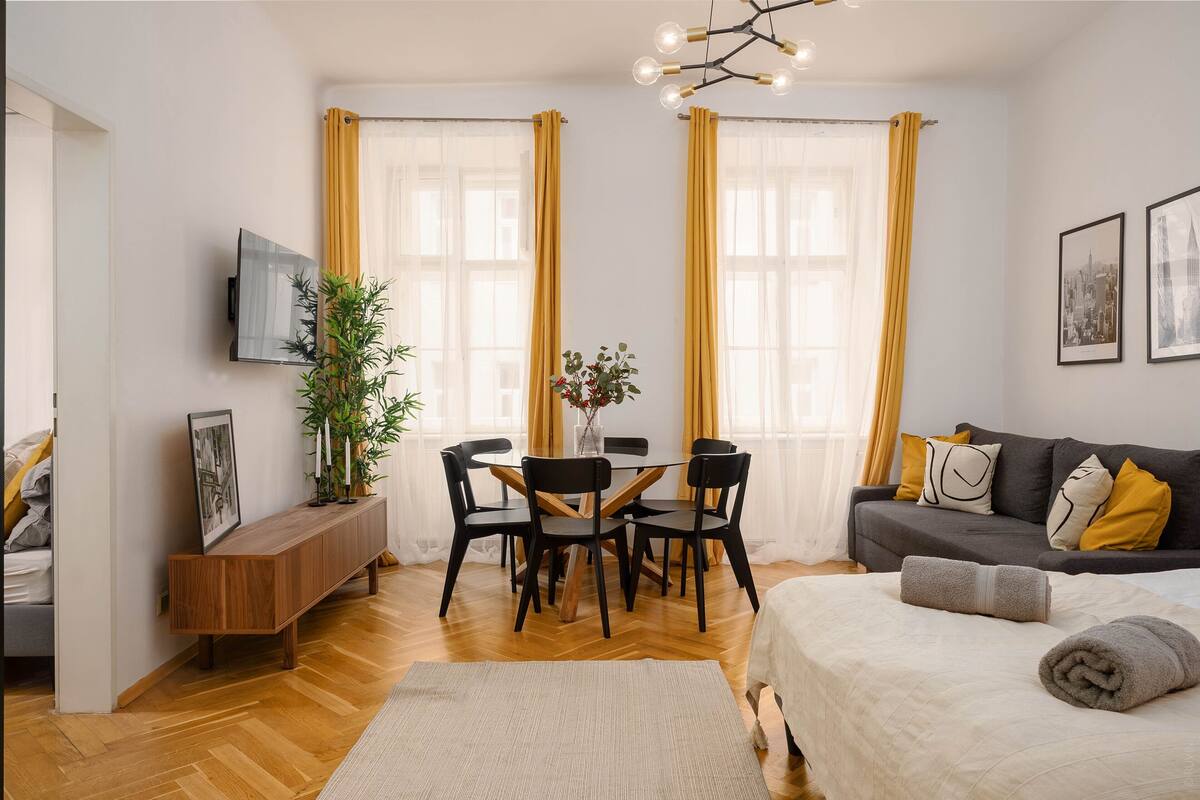 A modern living room with a dining area, a sofa, and a TV mounted on the wall.