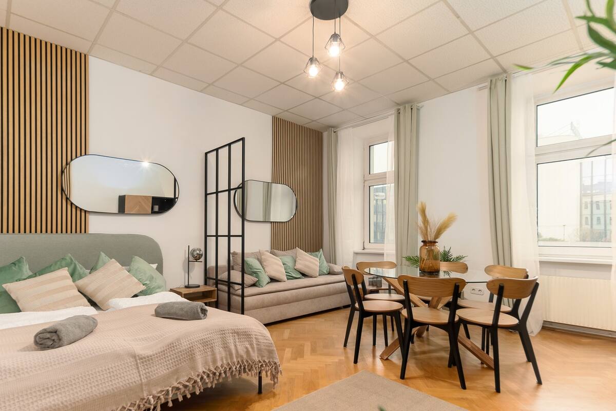 A modern bedroom with a bed, a sofa, a dining table with chairs, and a large window.