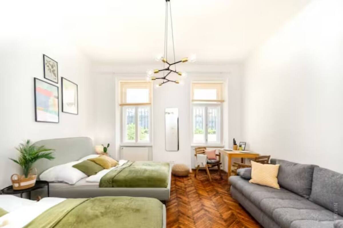A modern bedroom with two beds, a sofa, a dining table, and a large window.