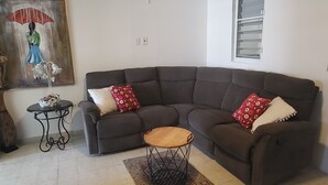 Una sala de estar con un sofá seccional marrón oscuro, una mesita de madera pequeña y un tapete estampado.